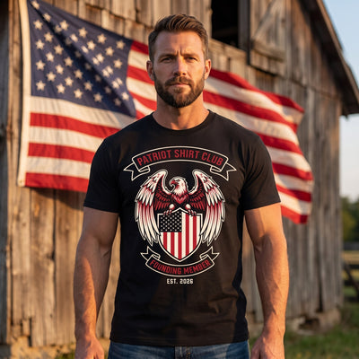Man wearing Patriot Shirt Club Founding Member black tee in front of an American flag and barn