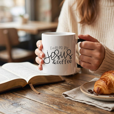 Hands holding Fueled by Jesus and Coffee mug over open Bible