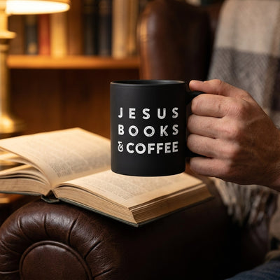 Hand holding black Jesus Books and Coffee mug beside open book